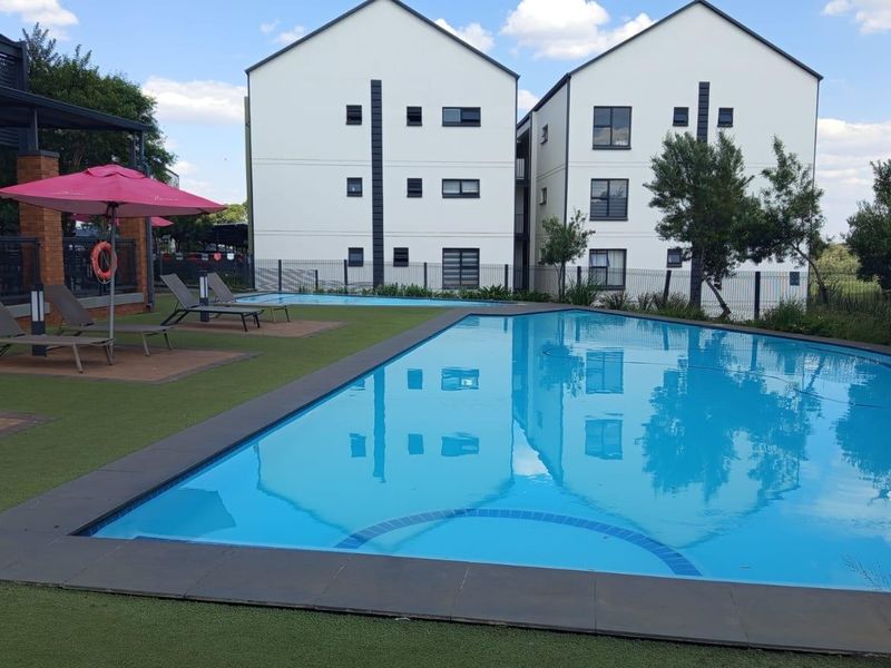 A well-maintained communal swimming pool area featuring artificial turf, paved surrounds, and views of the modern apartment complex.