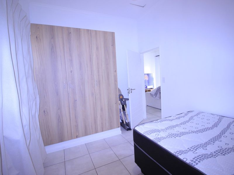 A bedroom featuring tiled flooring and a modern wood-finish built-in wardrobe, with an open doorway leading to an adjacent living area.