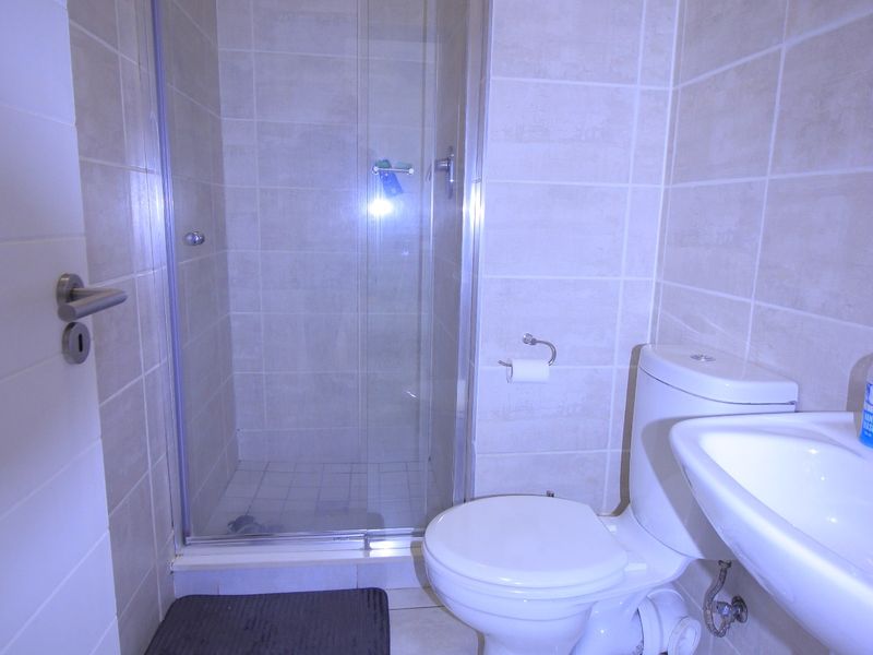 A clean, functional bathroom featuring a glass shower enclosure, pedestal basin, and toilet with neutral wall and floor tiling.