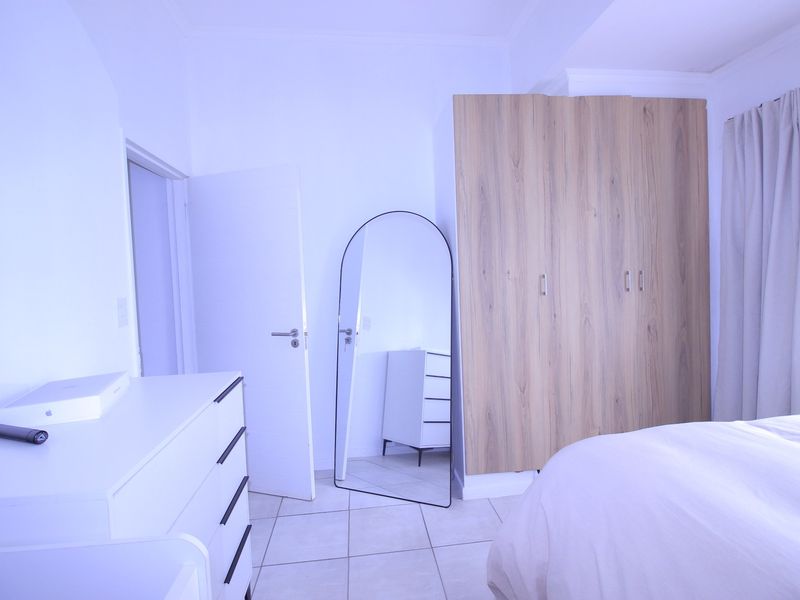 A well-maintained bedroom featuring light-toned built-in wardrobes, neutral tiled flooring, and clean white walls.