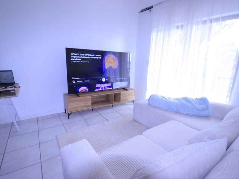 A bright living room featuring tiled flooring and a large sliding glass door with sheer curtains, providing ample natural light.