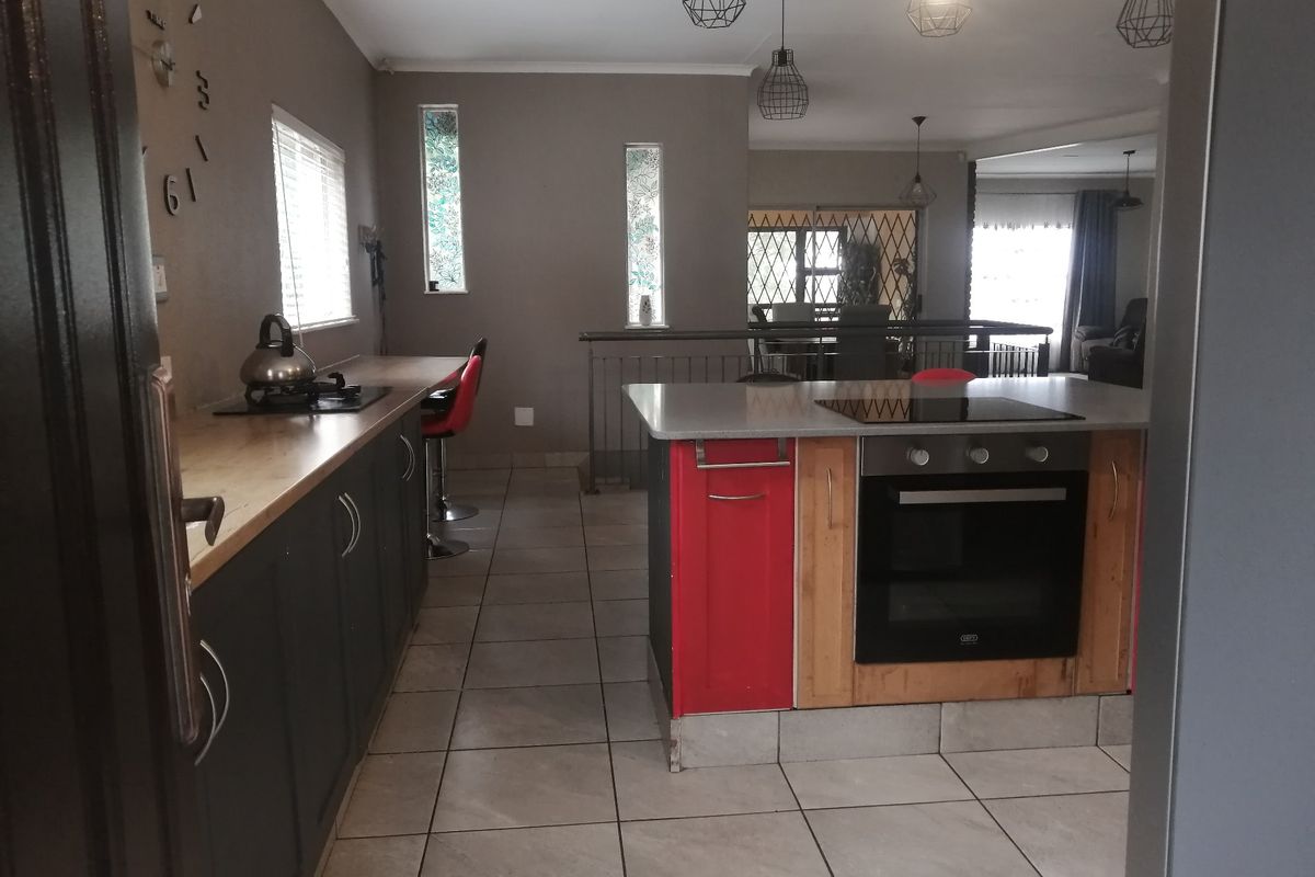 Modern kitchen featuring a central island with built-in oven and cooktop, tiled flooring, and open-plan layout connecting to the dining and living areas.