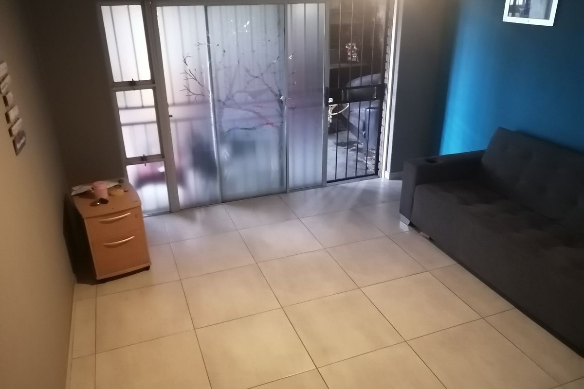 A living area featuring tiled flooring and a sliding glass door with an integrated security gate, providing access to the exterior.