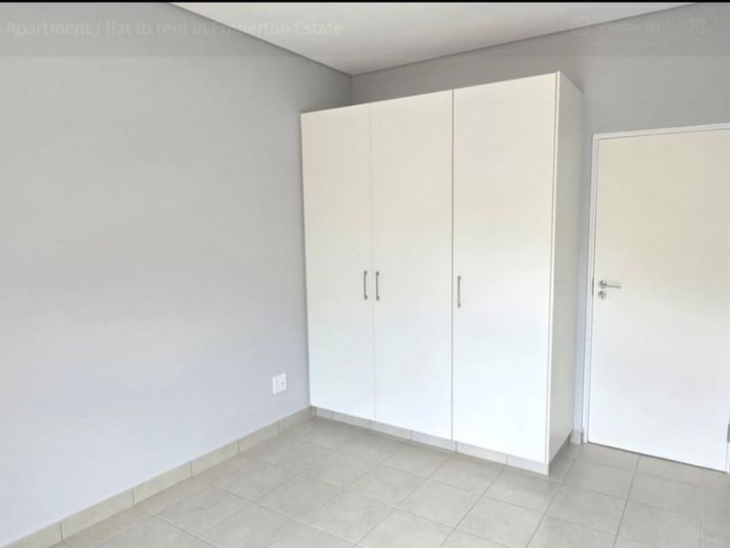A clean, neutral bedroom featuring built-in cupboards, tiled flooring, and a simple, modern finish.