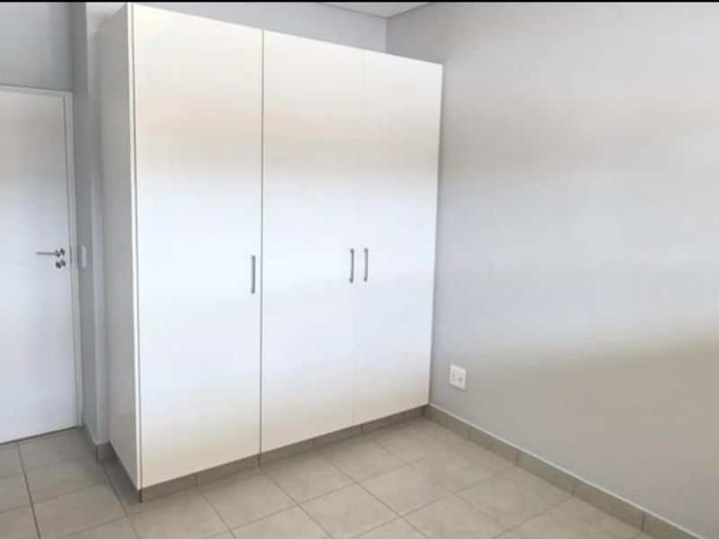 A clean, empty bedroom featuring neutral tiled flooring and a modern white built-in wardrobe.