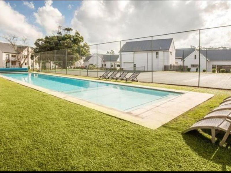 Communal outdoor area featuring a long swimming pool and adjacent tennis court, set within a well-maintained residential apartment complex.