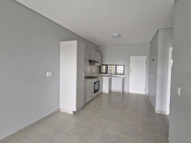 A clean, modern kitchen featuring neutral cabinetry, built-in oven and hob, and tiled flooring in an open-plan layout.