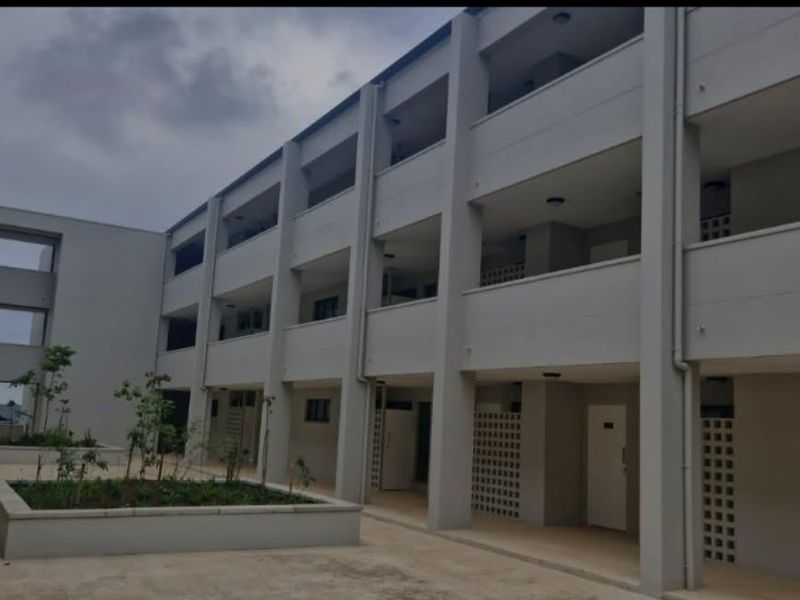 A view of the apartment complex exterior featuring multi-level balconies, concrete walkways, and integrated garden planters in the courtyard area.