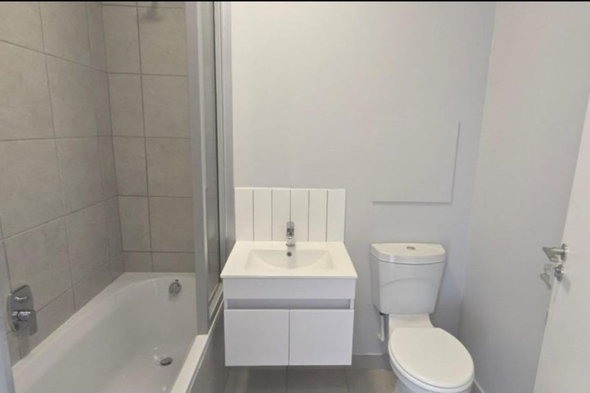 A clean, modern bathroom featuring a bathtub with a shower screen, a wall-mounted vanity with a basin, and a standard toilet.