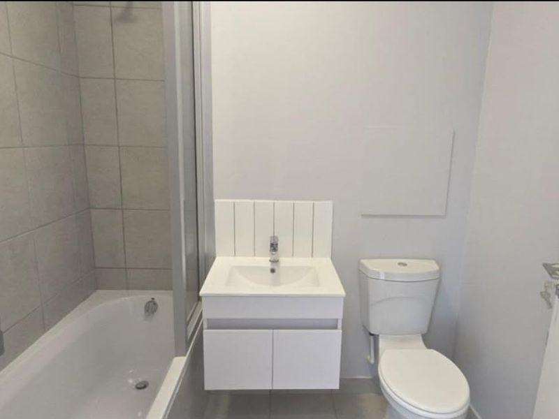 A clean, modern bathroom featuring a bathtub with a shower screen, a wall-mounted vanity with a basin, and a standard toilet.