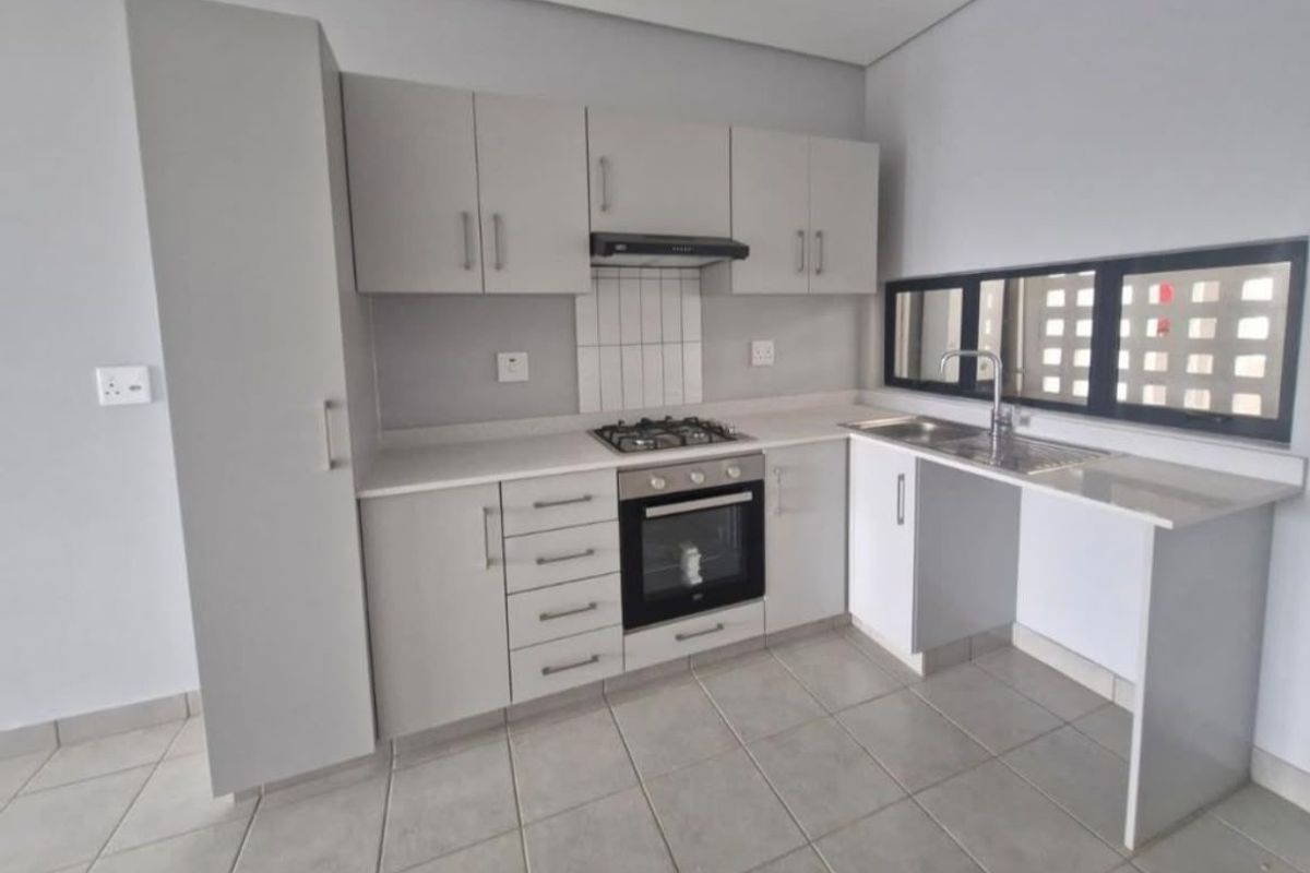 Modern kitchen featuring light grey cabinetry, built-in gas hob, oven, extractor fan, and tiled flooring with a clean, minimalist aesthetic.