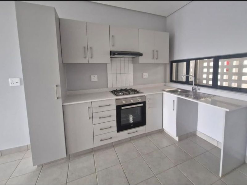 Modern kitchen featuring light grey cabinetry, built-in gas hob, oven, extractor fan, and tiled flooring with a clean, minimalist aesthetic.