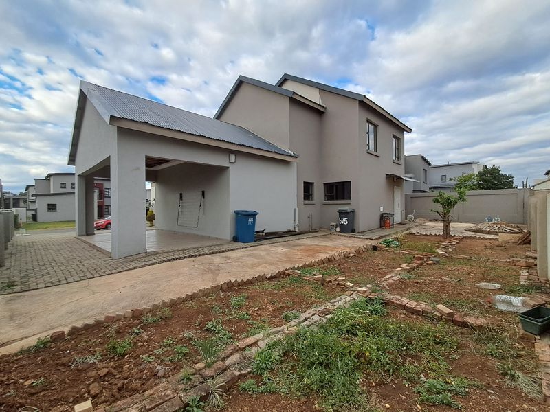 Rear view of the property featuring a covered carport, paved driveway, and an unlandscaped garden area with boundary walling.