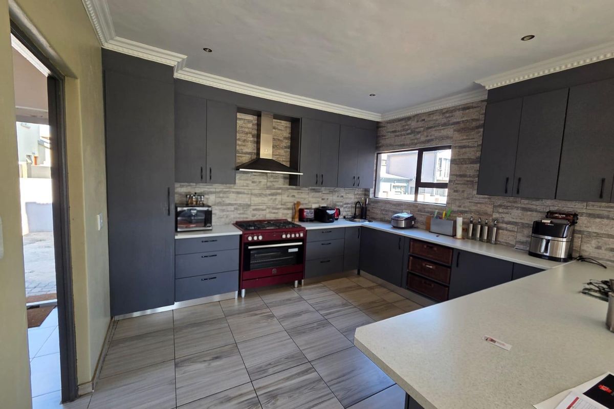 Modern kitchen featuring dark grey cabinetry, stone-look backsplash, gas stove with extractor fan, and light-toned tiled flooring.