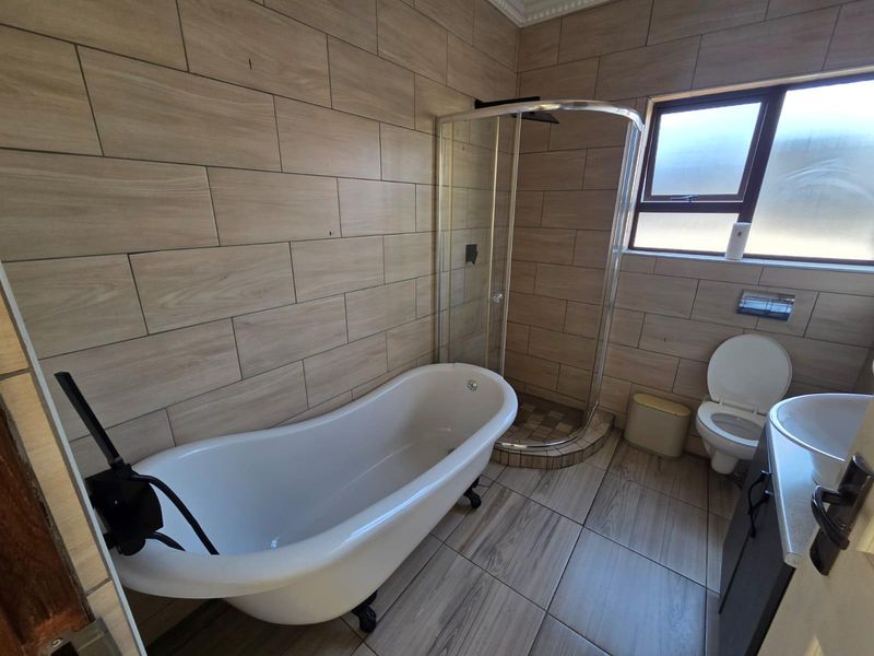 Modern bathroom featuring a freestanding bathtub, corner shower enclosure, wall-mounted toilet, and vanity basin with wood-look tiled walls and flooring.