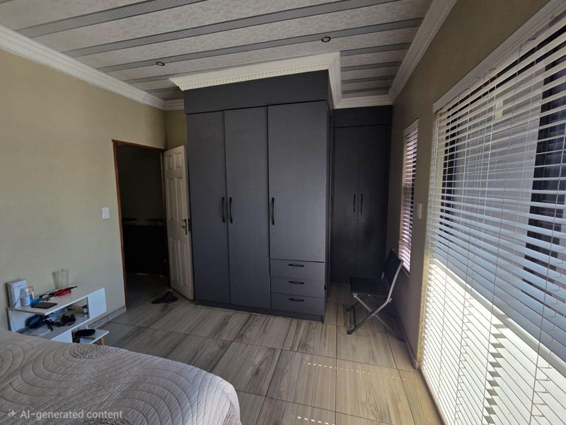 A bedroom featuring modern dark grey built-in cupboards, wood-look tiled flooring, and venetian blinds, offering a clean and functional living space.