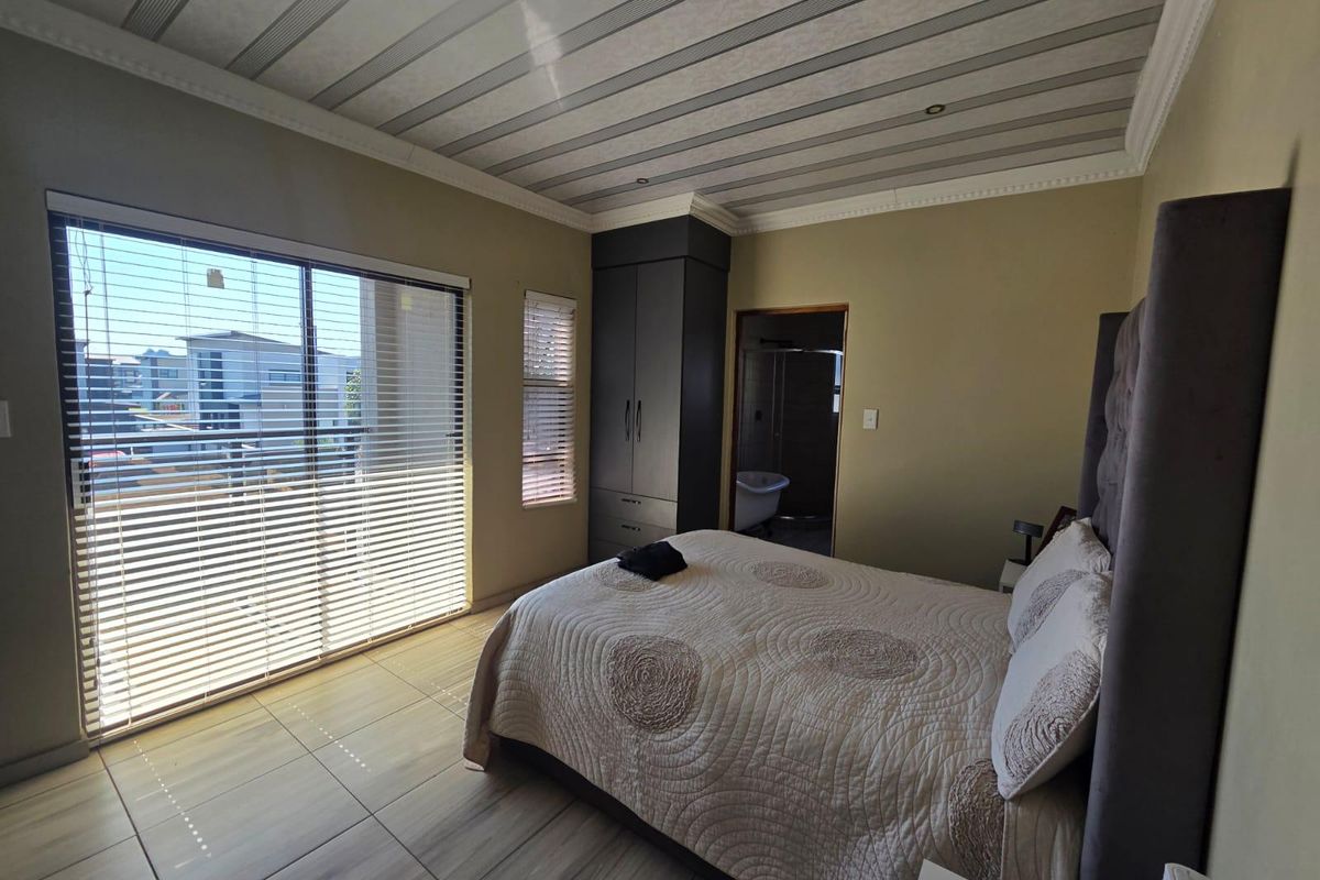 Spacious bedroom featuring tiled flooring, built-in wardrobe, decorative ceiling panels, and a sliding glass door leading to an outdoor balcony.