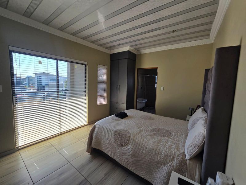 Spacious bedroom featuring tiled flooring, built-in wardrobe, decorative ceiling panels, and a sliding glass door leading to an outdoor balcony.