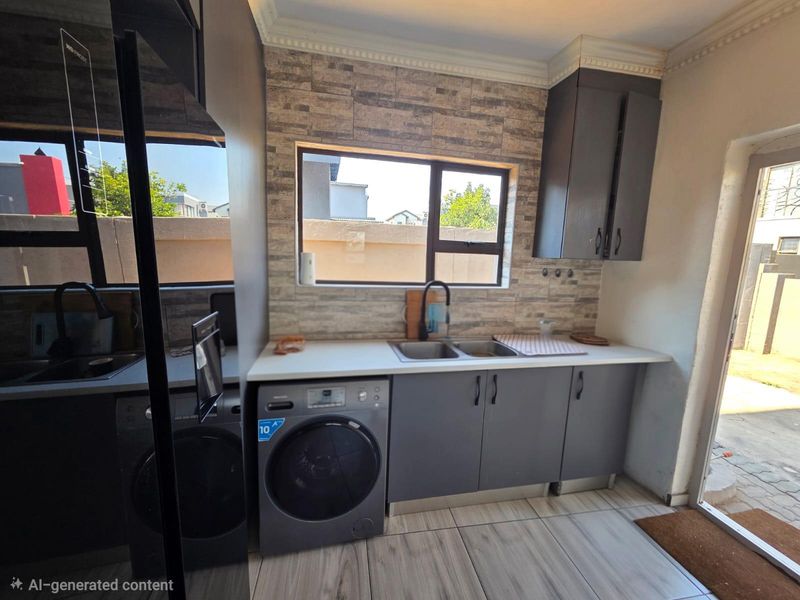A modern scullery featuring dark grey cabinetry, a double basin sink, stone-look splashback tiles, and wood-look flooring with direct access to the exterior.