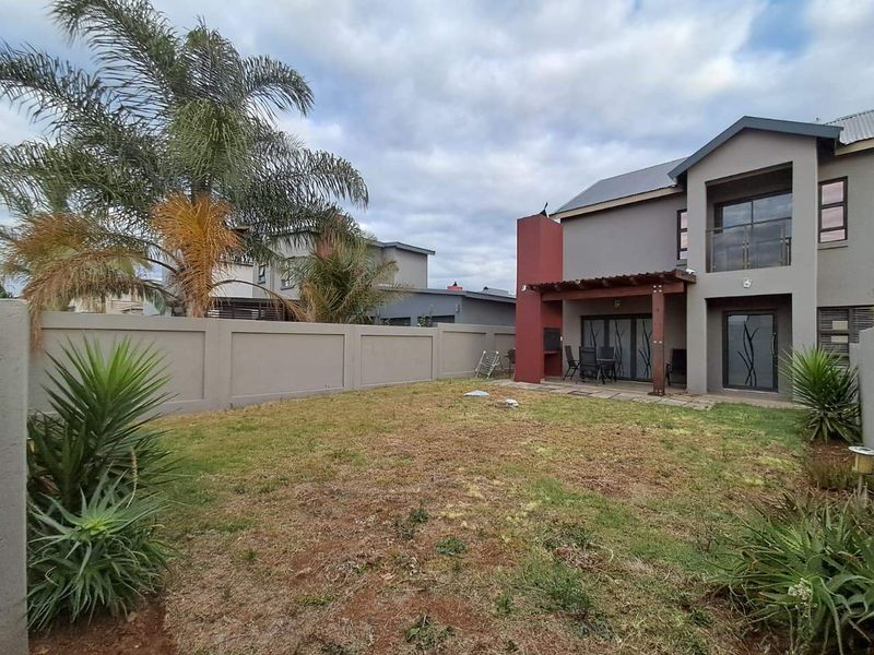 Rear view of a two-story house featuring a covered patio with a built-in braai, a timber pergola, and a private garden with perimeter walling.