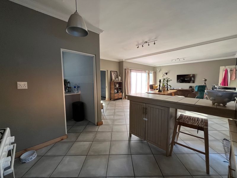 Spacious open-plan living area featuring tiled flooring, cove cornicing, and a breakfast bar, seamlessly connecting to the kitchen and outdoor access.