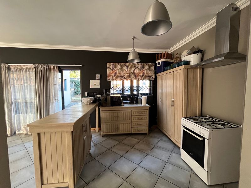 A functional kitchen featuring tiled flooring, built-in wooden cabinetry, a gas stove with extractor fan, and a breakfast bar with access to the patio.
