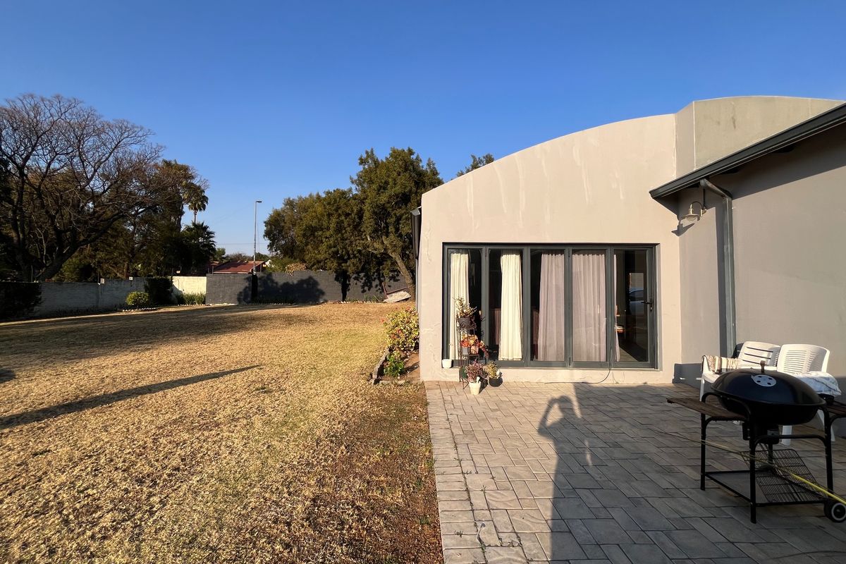 Rear view of the townhouse featuring a paved patio area, large bi-fold doors, and a spacious garden with boundary walling.