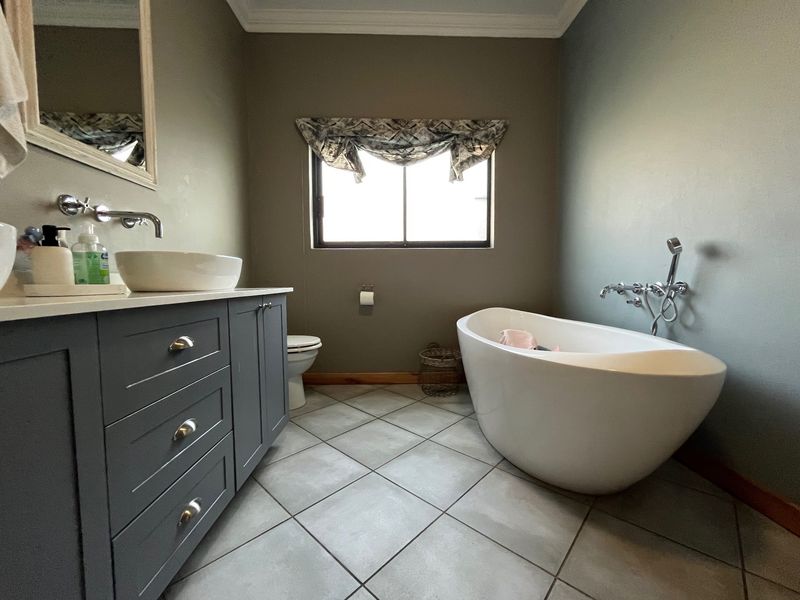 A well-appointed bathroom featuring a modern freestanding bathtub, a dark grey vanity with a vessel sink, and neutral tiled flooring.