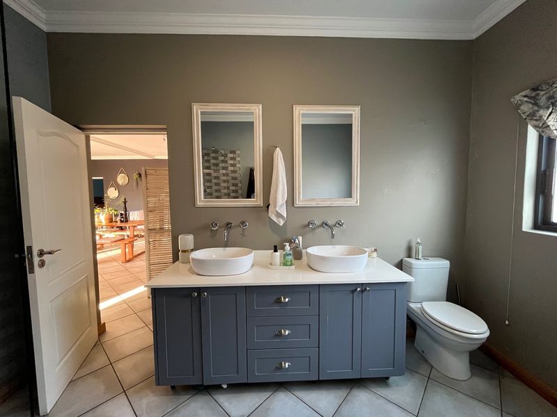 A well-appointed bathroom featuring a modern double vanity with vessel sinks, wall-mounted faucets, dual mirrors, and a clean, neutral aesthetic.