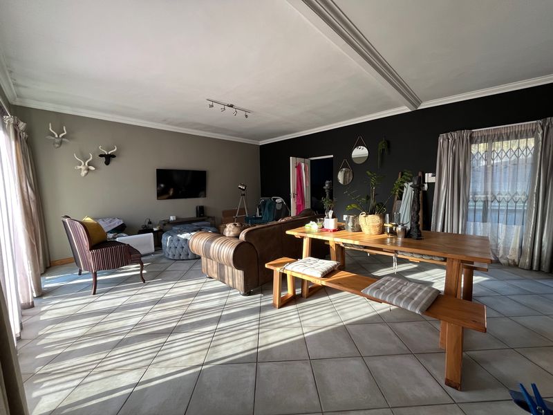 Spacious open-plan living and dining area featuring large ceramic floor tiles, natural light through sliding glass doors, and a modern accent wall.