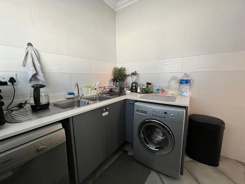A functional laundry area featuring built-in cabinetry, a stainless steel sink, and tiled splashback, providing practical utility space for household tasks.