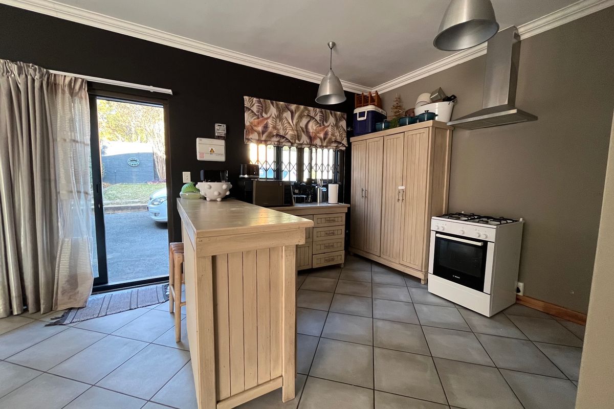 A functional kitchen featuring tiled flooring, a gas stove with extractor fan, built-in cabinetry, and a breakfast counter with direct access to the exterior.