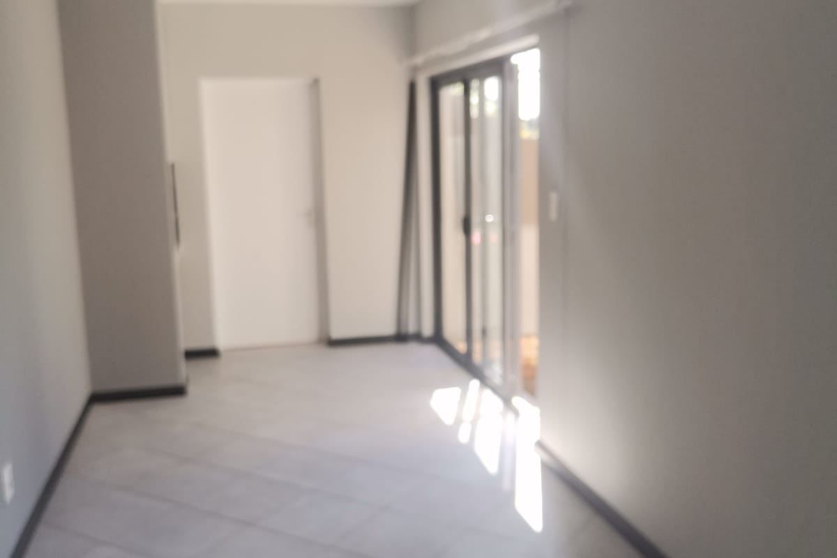 An empty, neutrally painted living area featuring tiled flooring and sliding glass doors that provide access to an outdoor space.