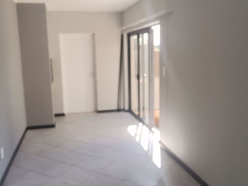 An empty, neutrally painted living area featuring tiled flooring and sliding glass doors that provide access to an outdoor space.
