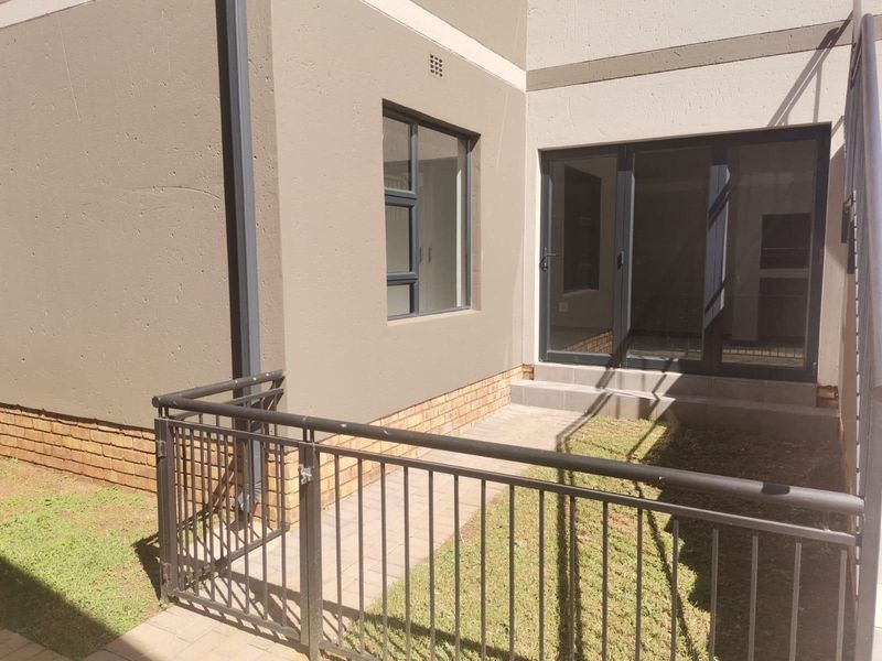 Rear exterior view of the apartment featuring a paved walkway, metal security railing, and sliding glass door access to the interior.