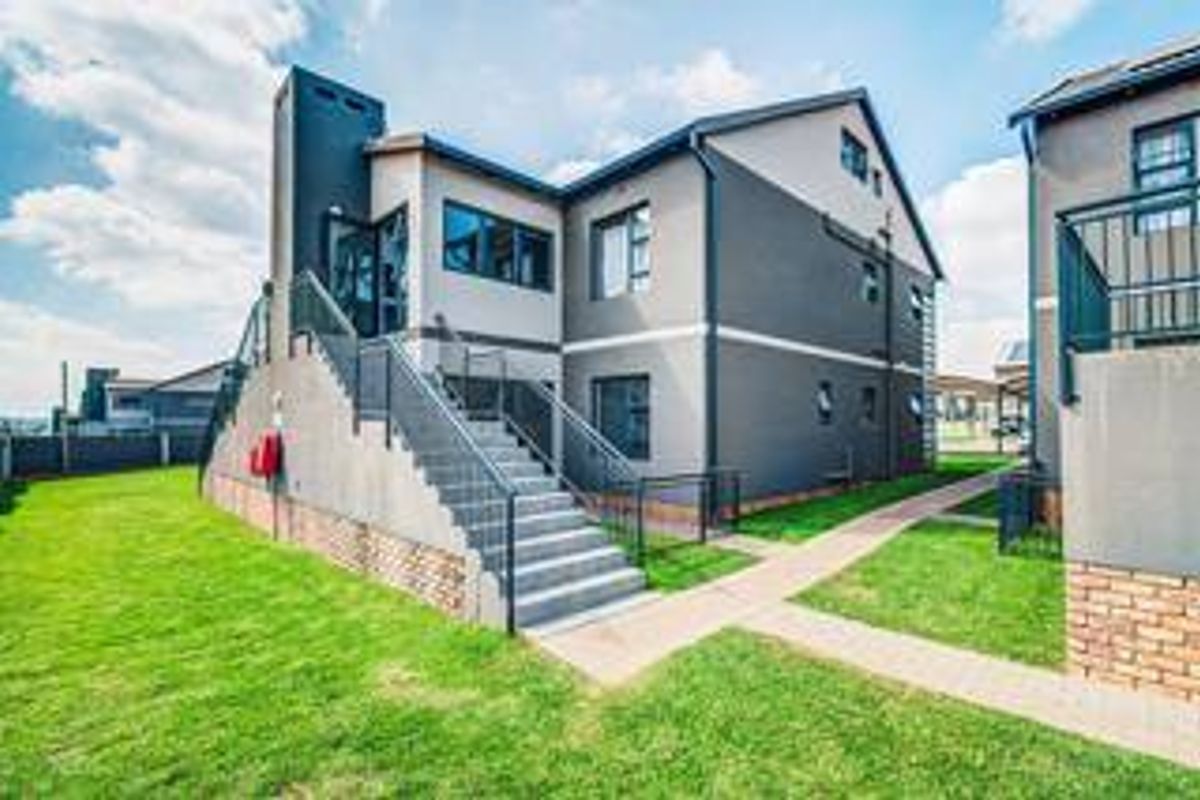 Rear view of a modern apartment building featuring an external staircase, metal railings, and a well-maintained lawn with paved walkways.