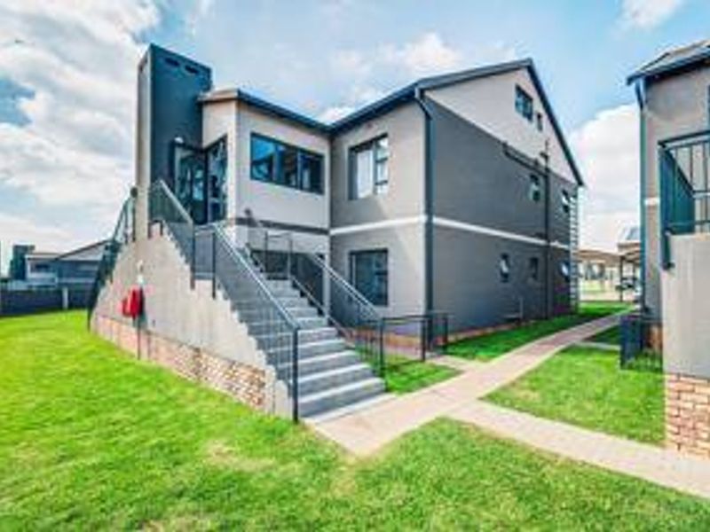 Rear view of a modern apartment building featuring an external staircase, metal railings, and a well-maintained lawn with paved walkways.