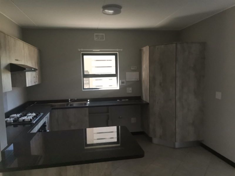 A clean, modern kitchen featuring built-in cabinetry, dark laminate countertops, a gas hob with extractor fan, and a double sink.