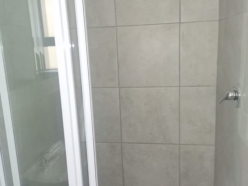 A clean, modern shower stall featuring neutral-toned wall tiles and a glass enclosure.