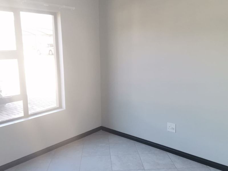 A bright, empty bedroom featuring neutral grey walls, tiled flooring, and a large aluminium window providing natural light.