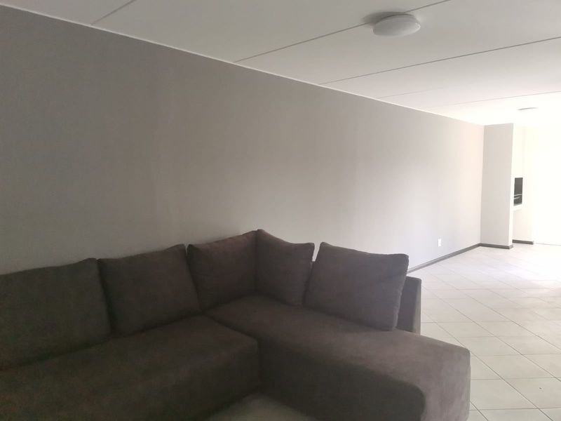 A spacious living area featuring neutral wall tones and tiled flooring, leading into an adjacent kitchen space.