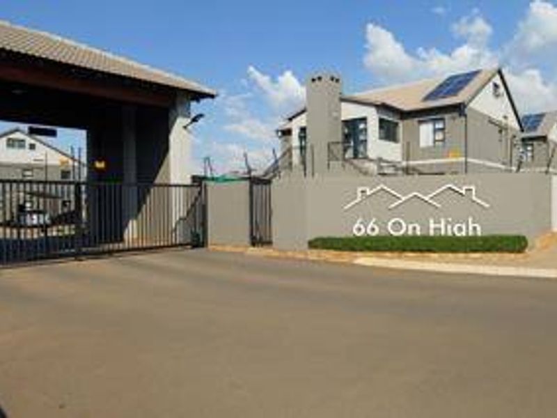 The entrance to 66 On High apartment complex, featuring a secure gated access point, perimeter walling, and modern residential buildings with solar panels.
