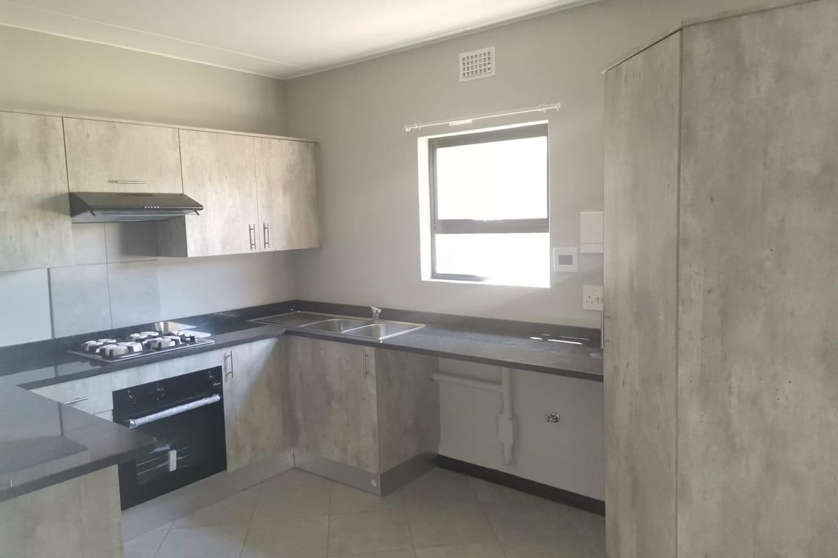 Modern kitchen featuring light wood-look cabinetry, dark stone countertops, built-in gas hob, oven, and extractor fan with tiled flooring.