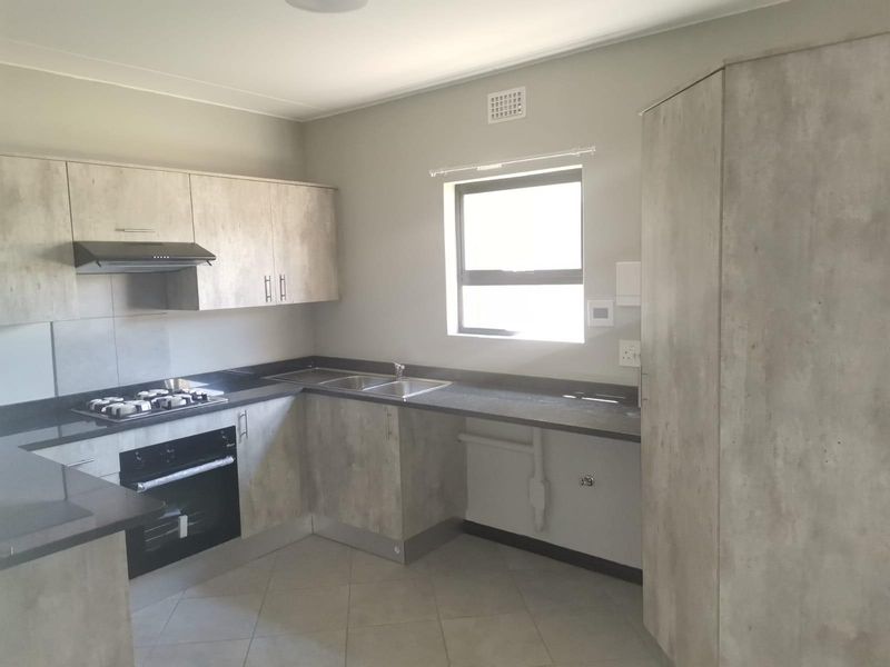 Modern kitchen featuring light wood-look cabinetry, dark stone countertops, built-in gas hob, oven, and extractor fan with tiled flooring.