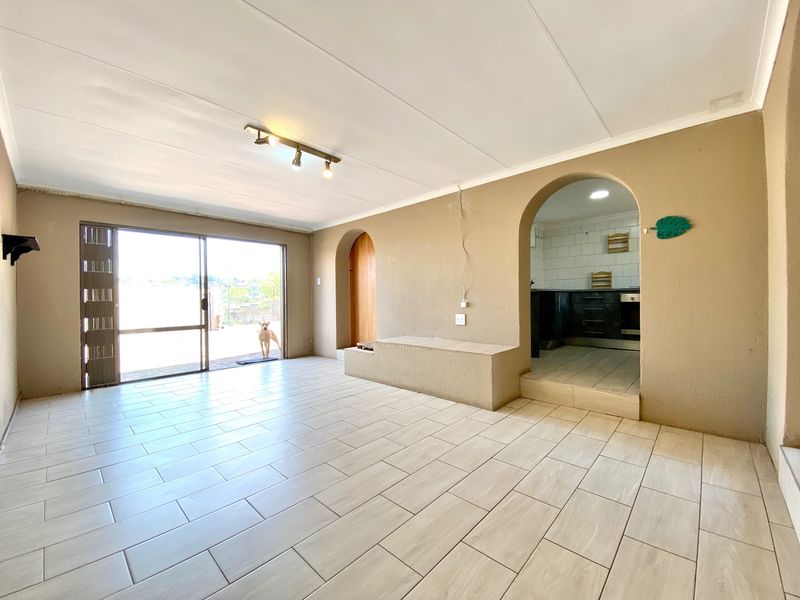 Spacious open-plan living area featuring tiled flooring, an arched entryway to the kitchen, and a large sliding door leading to the outdoor space.