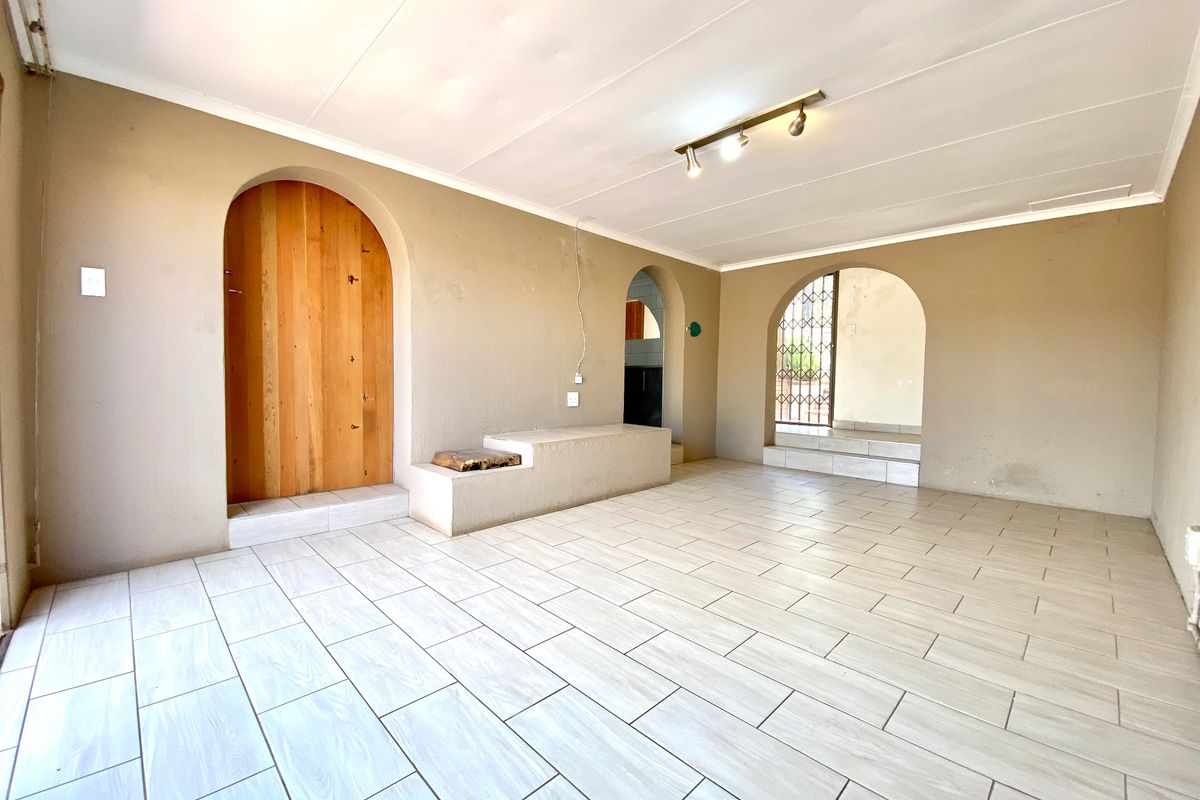 An empty living area featuring light-toned tiled flooring, distinctive arched doorways, and a built-in concrete bench, offering a neutral canvas for interior design.