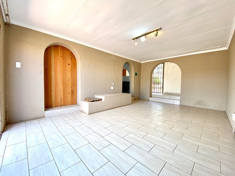 An empty living area featuring light-toned tiled flooring, distinctive arched doorways, and a built-in concrete bench, offering a neutral canvas for interior design.