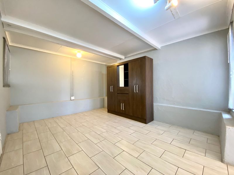 A bedroom featuring light-toned tiled flooring, exposed ceiling beams, and a built-in wardrobe, offering a neutral canvas for interior design.