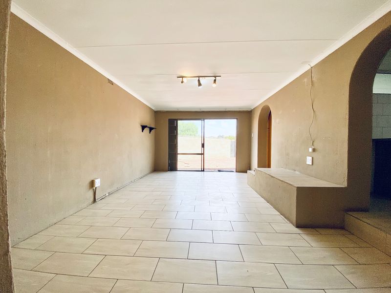 An empty, open-plan living area featuring tiled flooring, a built-in masonry bench, and a sliding glass door leading to the exterior.
