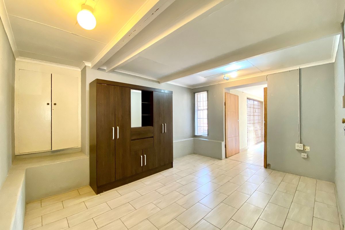 A bedroom featuring tiled flooring, built-in storage, and exposed ceiling beams, leading to an adjacent hallway with a security gate.